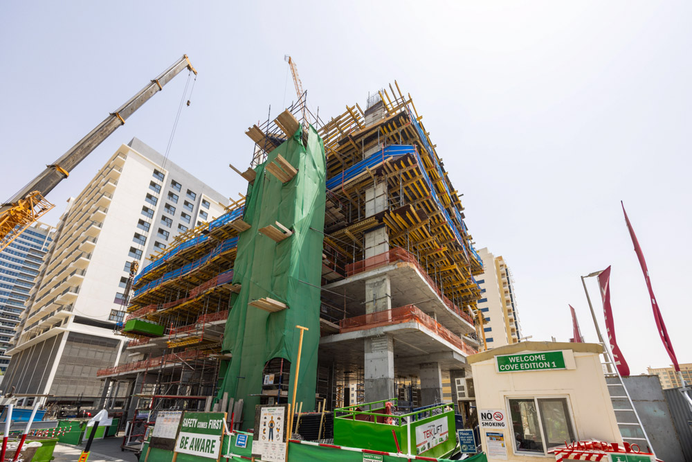 Cove Edition I By Imtiaz 1 A large construction site featuring a building under development, cranes, scaffolding, and safety signage.